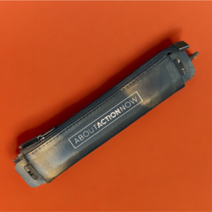 Black pencil case with the text "ABOUT ACTION NOW" lying on an orange surface.