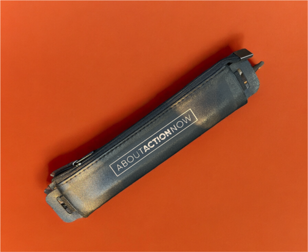 Black pencil case with the text "ABOUT ACTION NOW" lying on an orange surface.