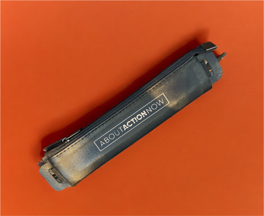 Black pencil case with the text "ABOUT ACTION NOW" lying on an orange surface.